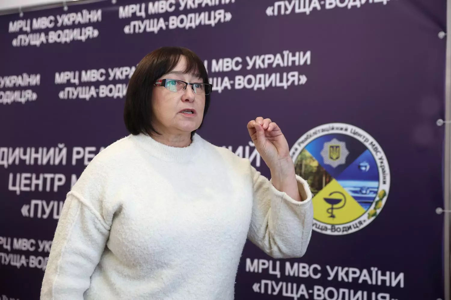 Жінка в білому светрі виступає на фоні банера медичного реабілітаційного центру МВС України