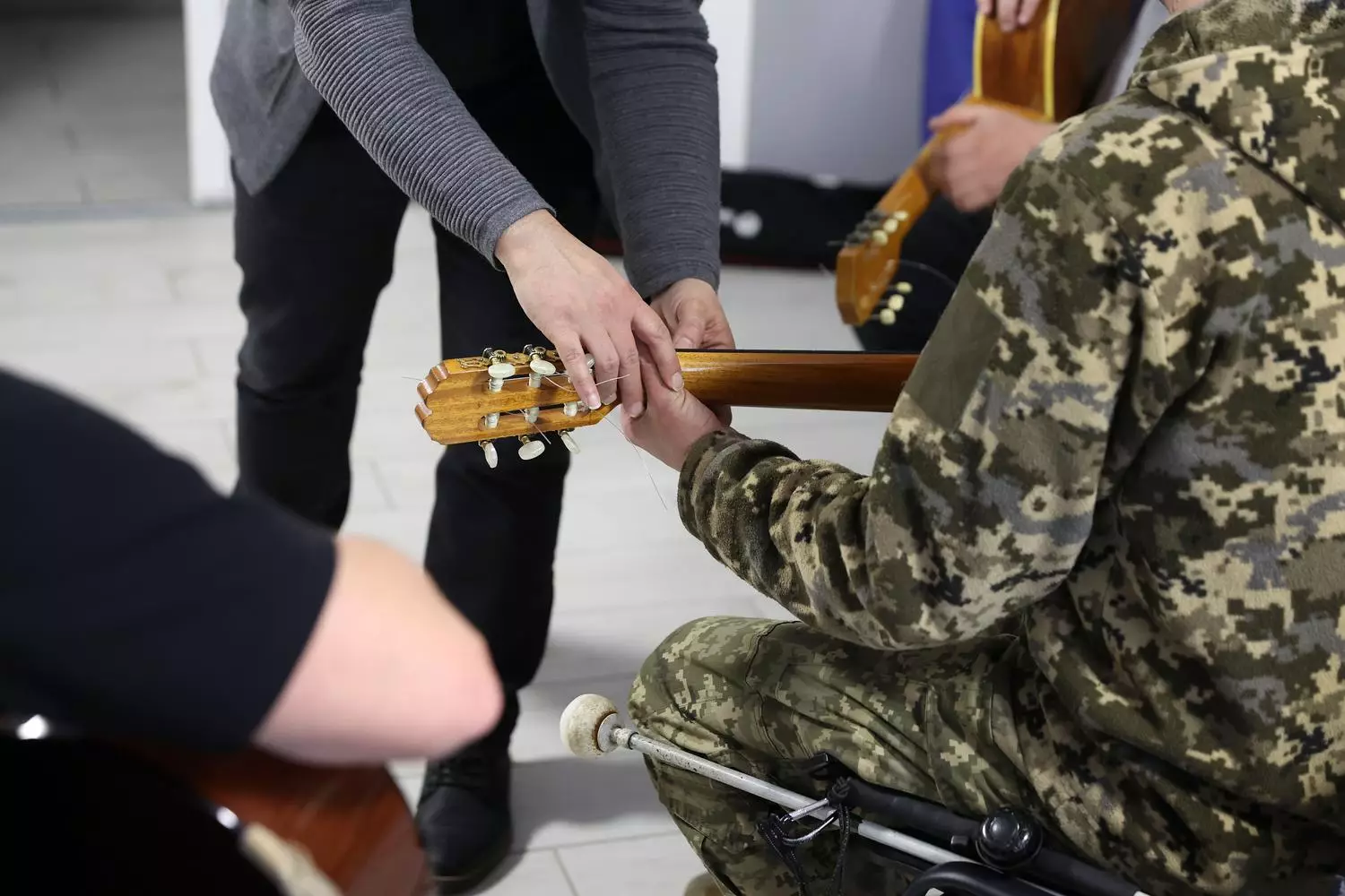 Людина в камуфляжі вчиться грати на гітарі під керівництвом інструктора в реабілітаційному центрі