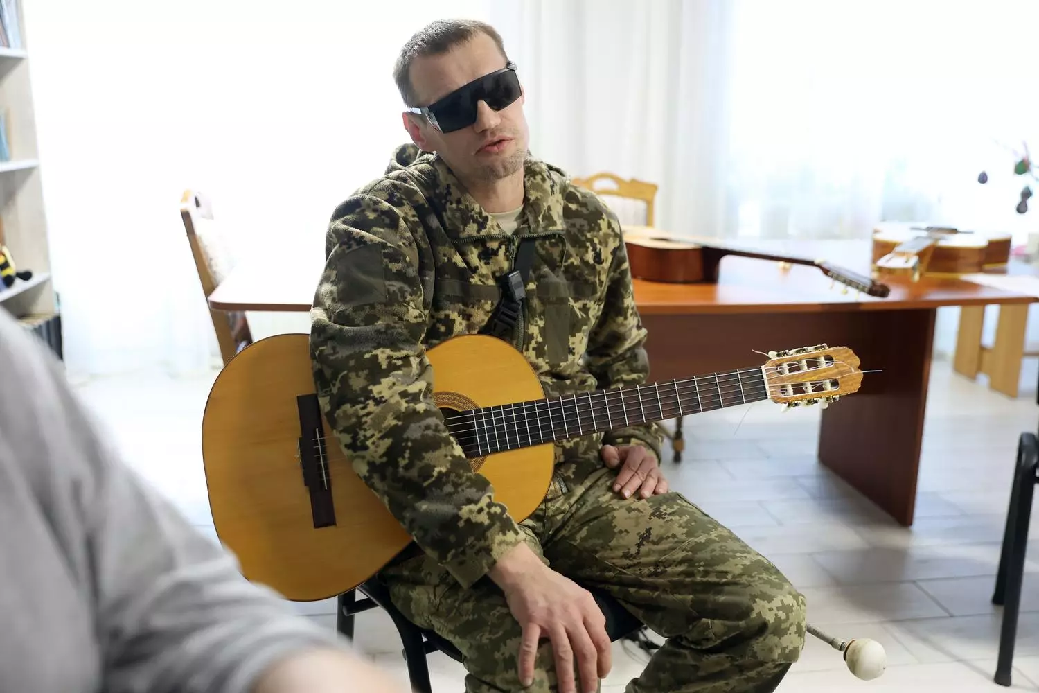 Ветеран у камуфляжі грає на гітарі в реабілітаційному центрі, підтримуючи відновлення через музику
