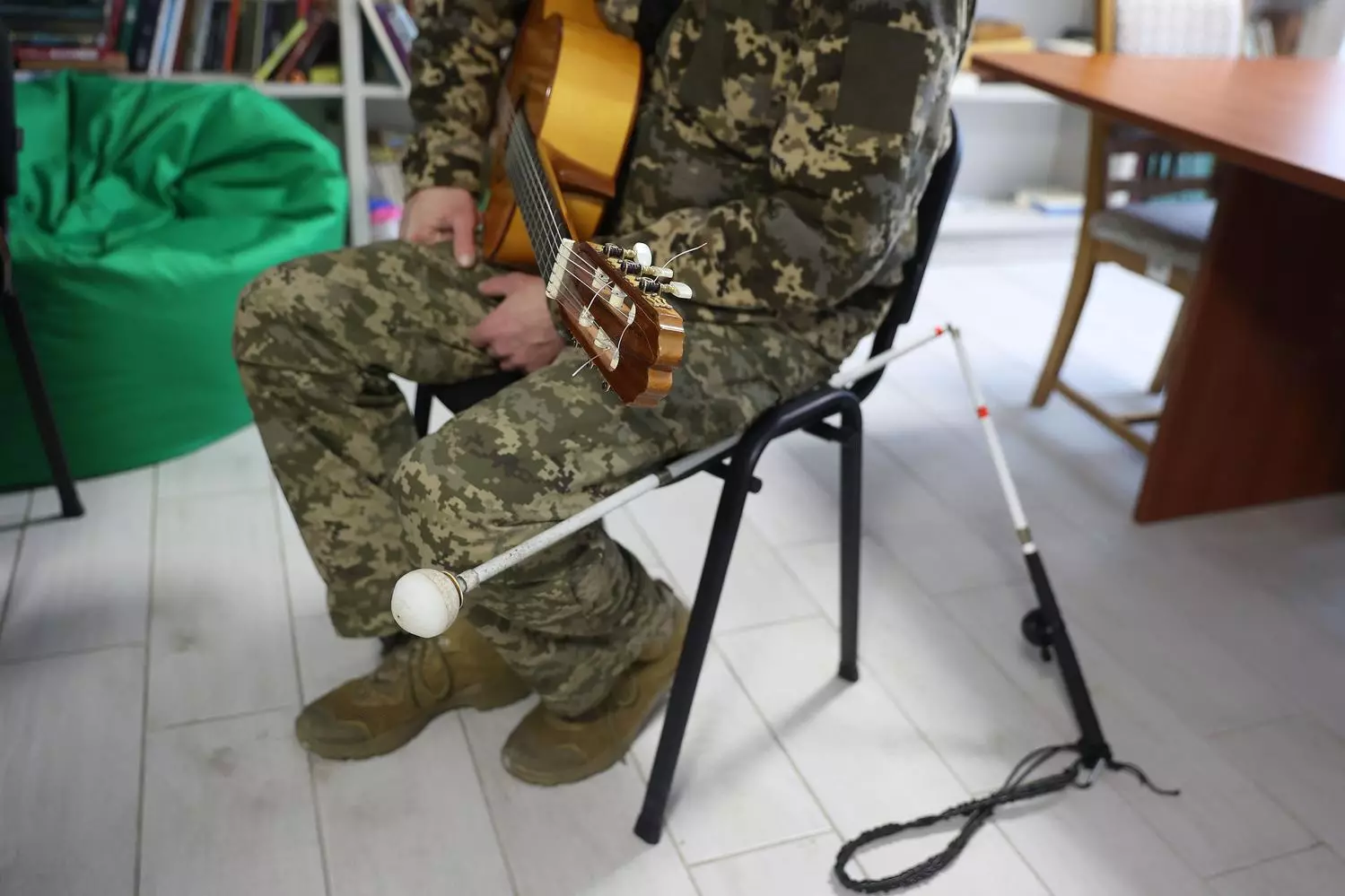 Ветеран у камуфляжі грає на гітарі в реабілітаційному центрі, поруч лежить біла тростина