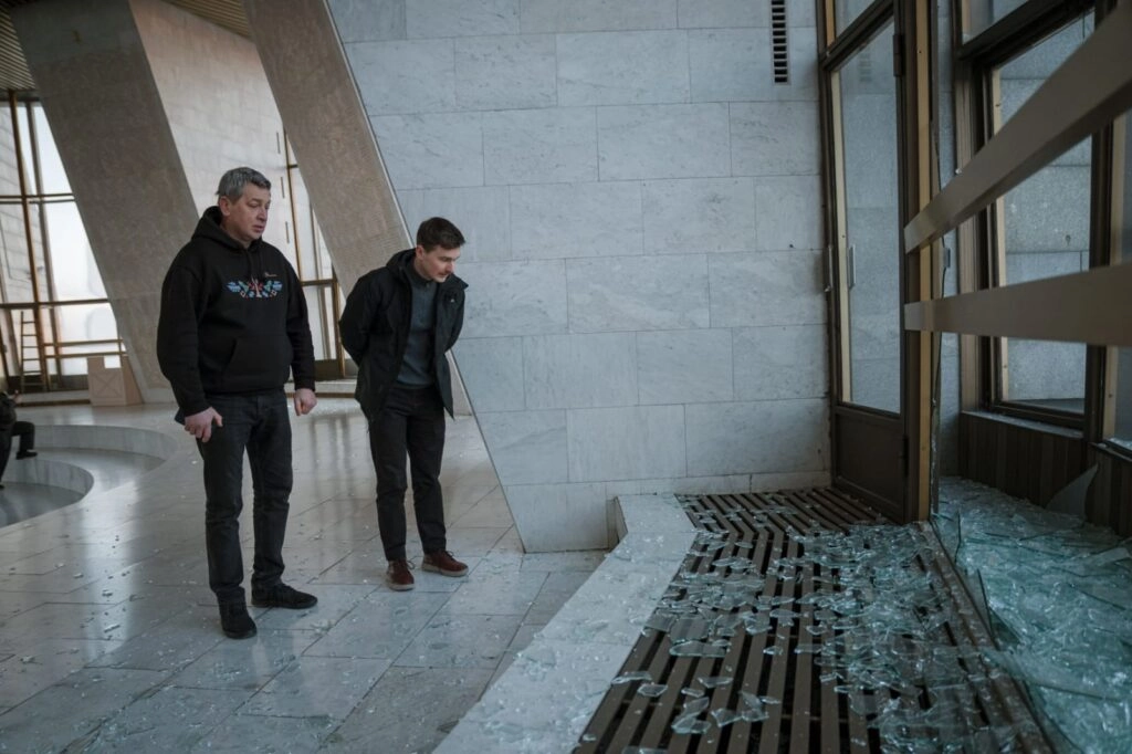 Двоє чоловіків оглядають розбиті вікна та уламки скла в залі музею після ракетного обстрілу