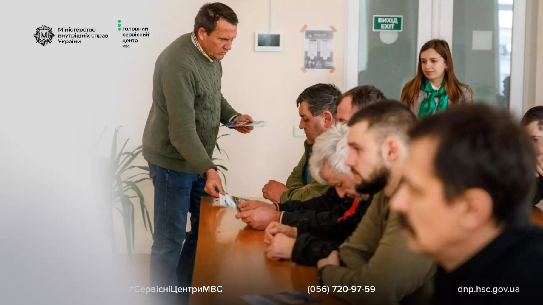 Чоловік роздає документи групі людей у приміщенні сервісного центру МВС