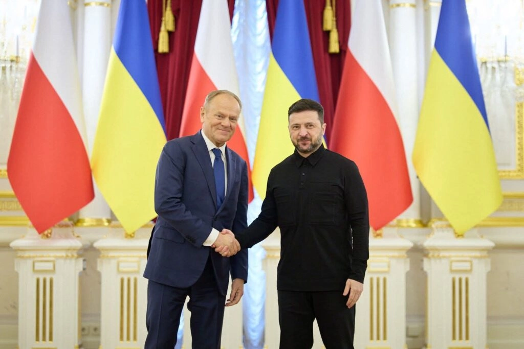 Президент України Зеленський і Прем’єр-міністр Польщі Туск тиснуть руки на тлі прапорів України та Польщі