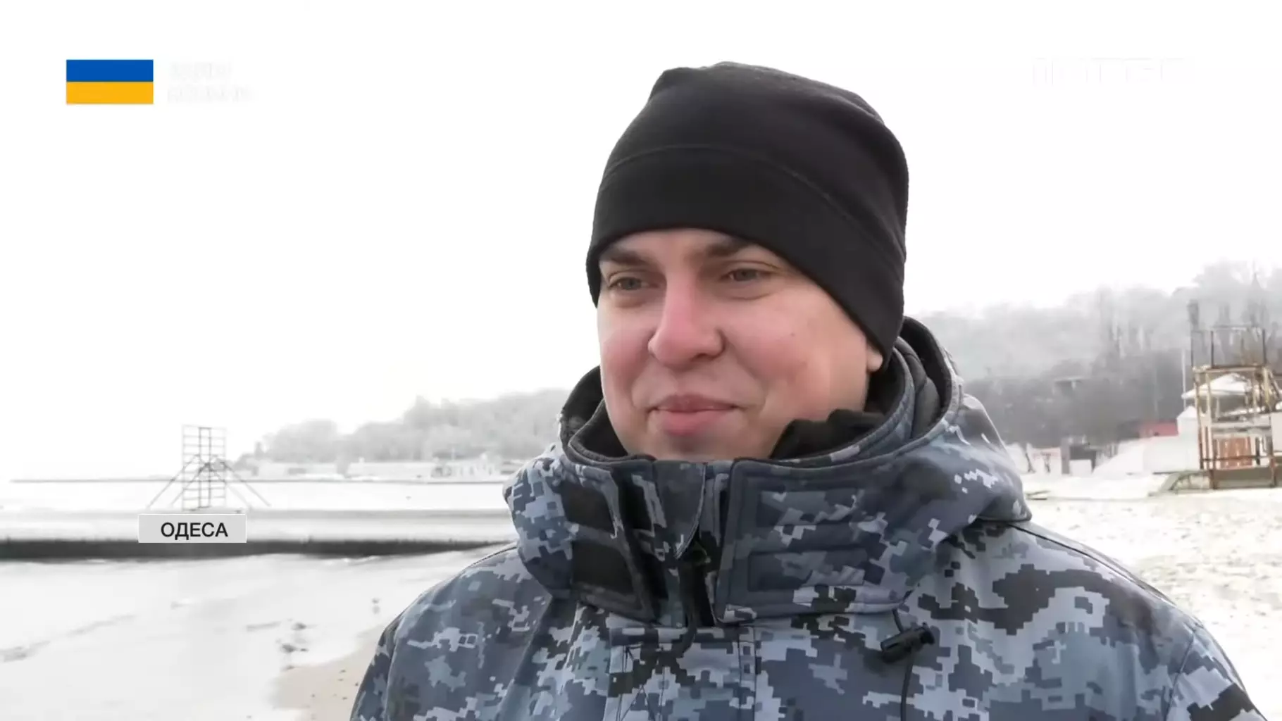 Прикордонник у зимовій формі на тлі засніженого пляжу в Одесі, усміхається на камеру