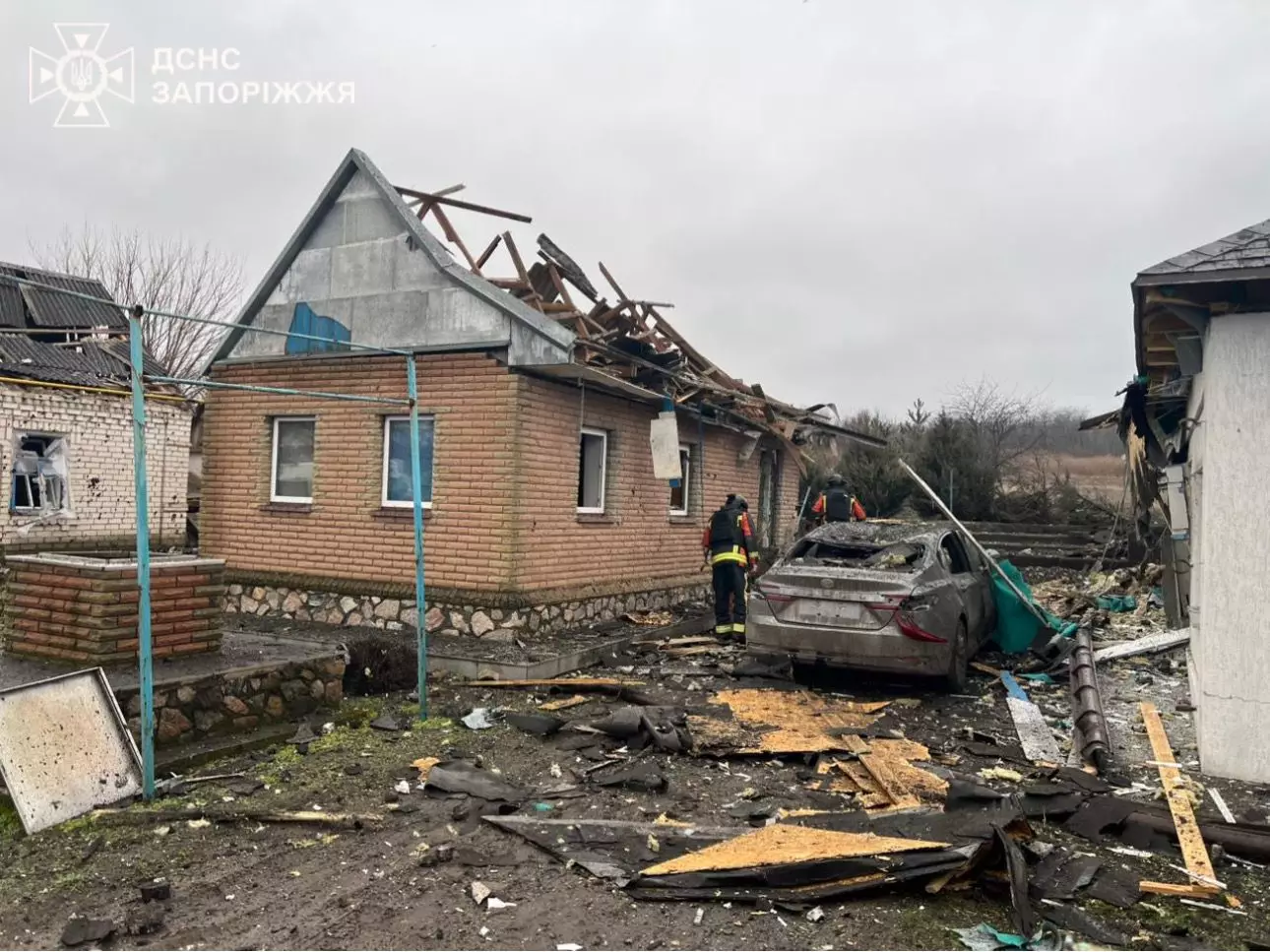 Рятувальники оглядають пошкоджений будинок після обстрілу, зруйнований дах, розбите авто на подвір'ї
