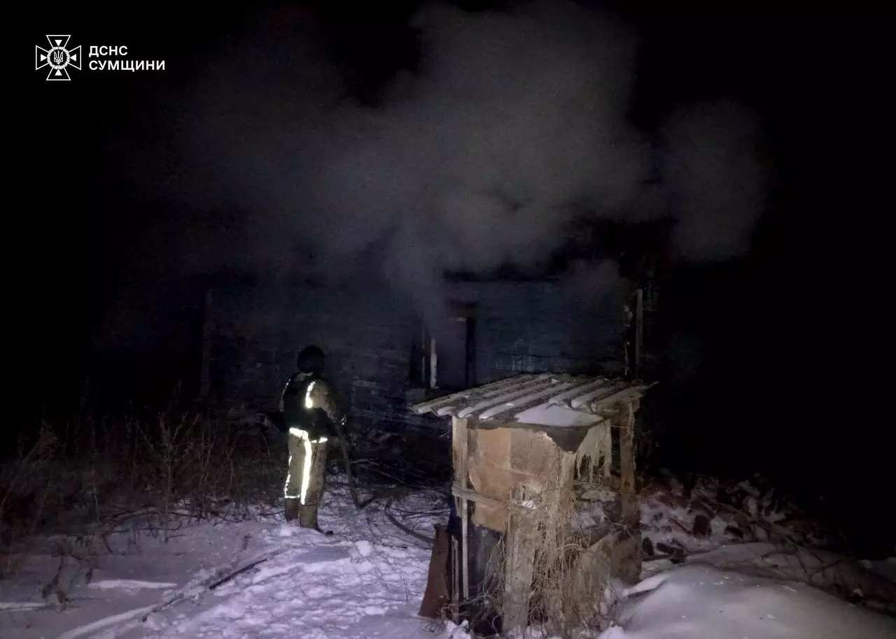 Пожежник у нічний час гасить палаючу будівлю після обстрілів, дим піднімається в темне небо