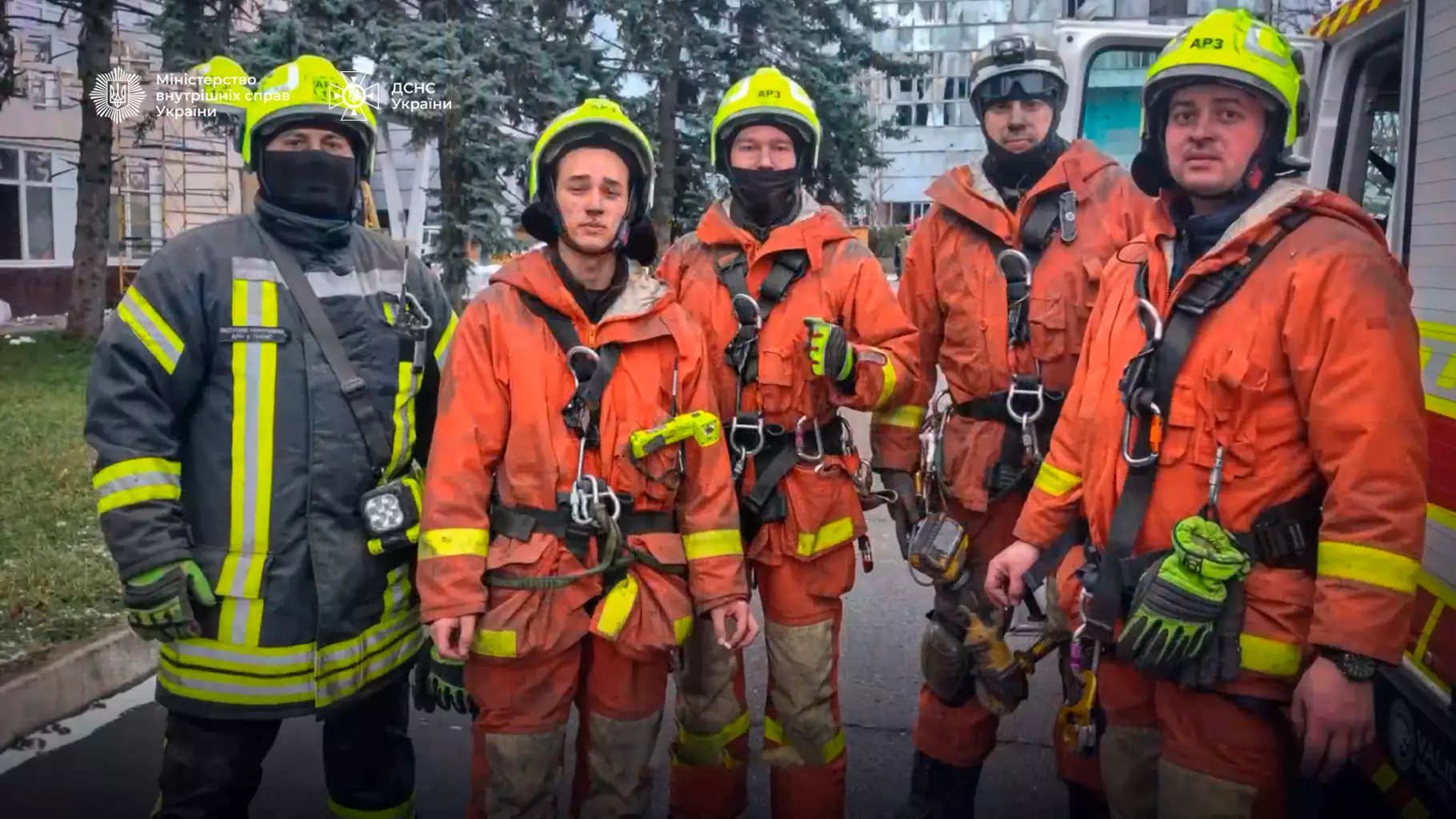 Рятувальники ДСНС у захисному спорядженні стоять перед пожежною машиною на тлі міської забудови